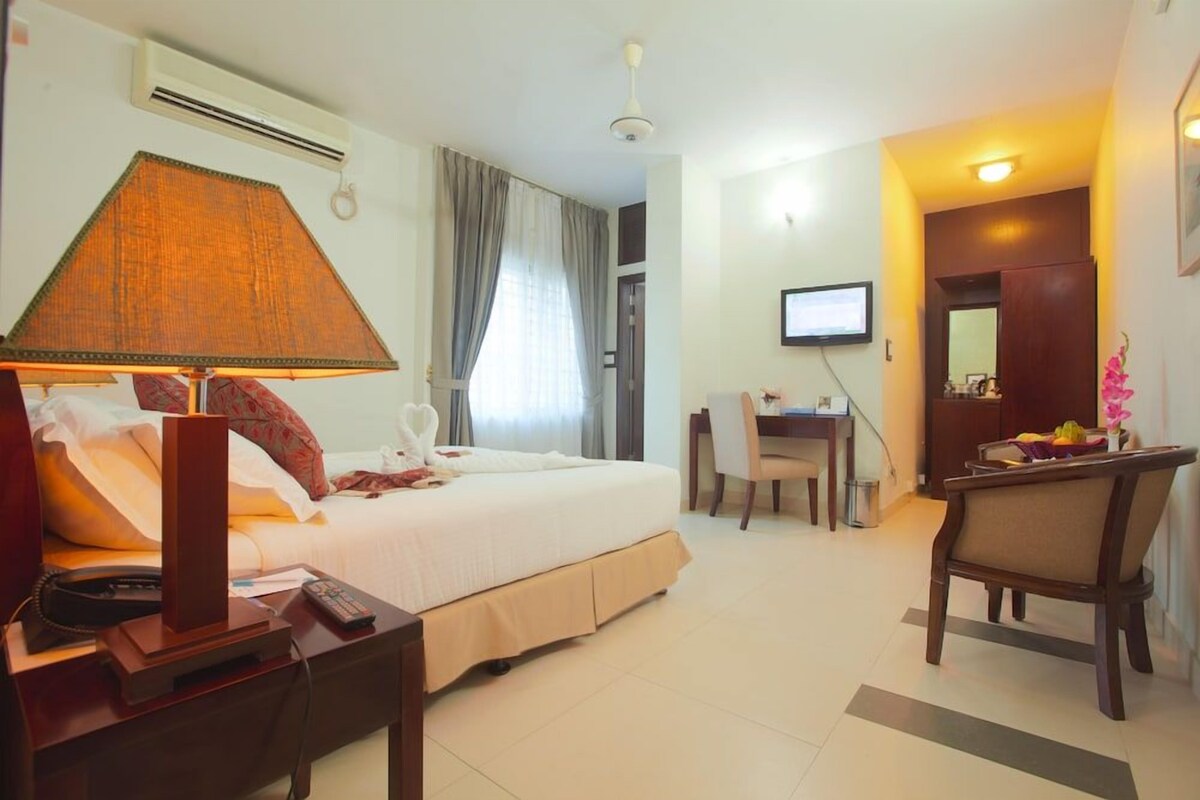 A hotel room with a bed, bedside table, lamp, desk, chair, and a television.