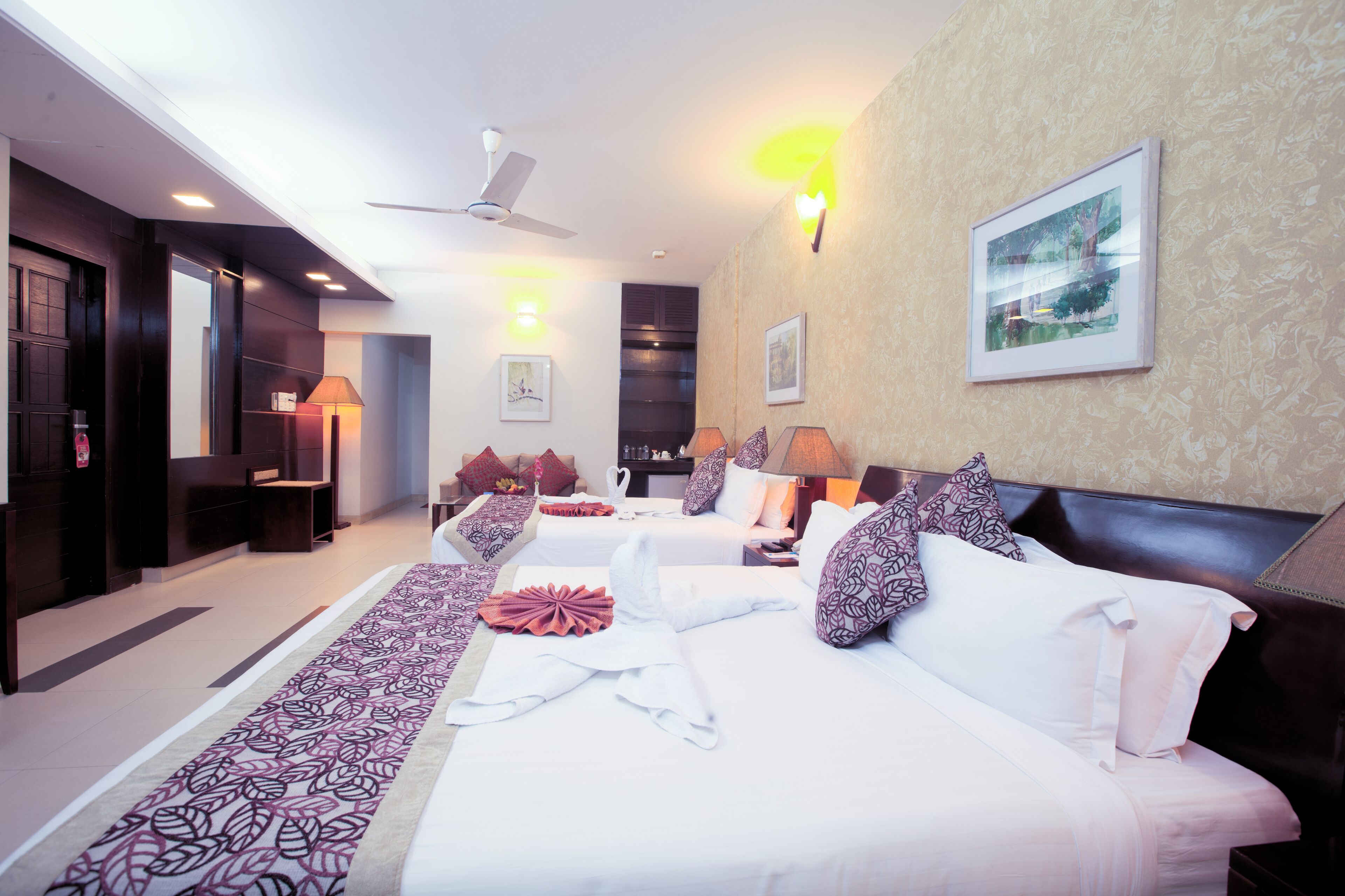 Une chambre d’hôtel avec un grand lit, un lit plus petit, un canapé, un bureau et un ventilateur de plafond.
