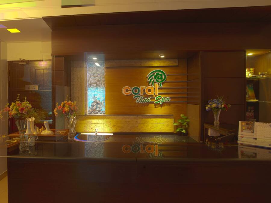 A reception area with a wooden counter, a neon sign for Coral Thai Spa, and decorative vases with flowers.