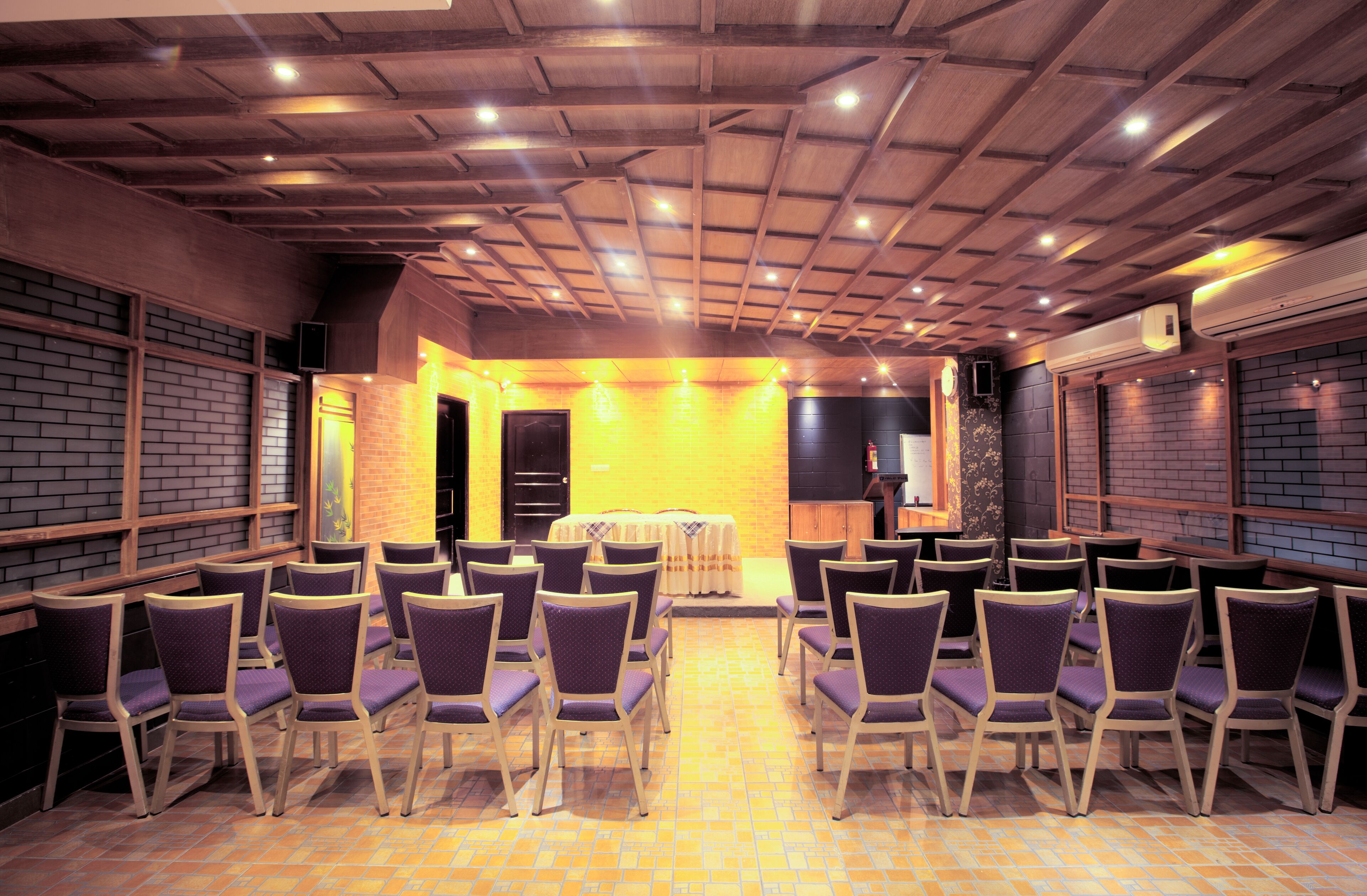 A conference room with rows of chairs facing a stage, wooden ceiling beams, and brick walls.