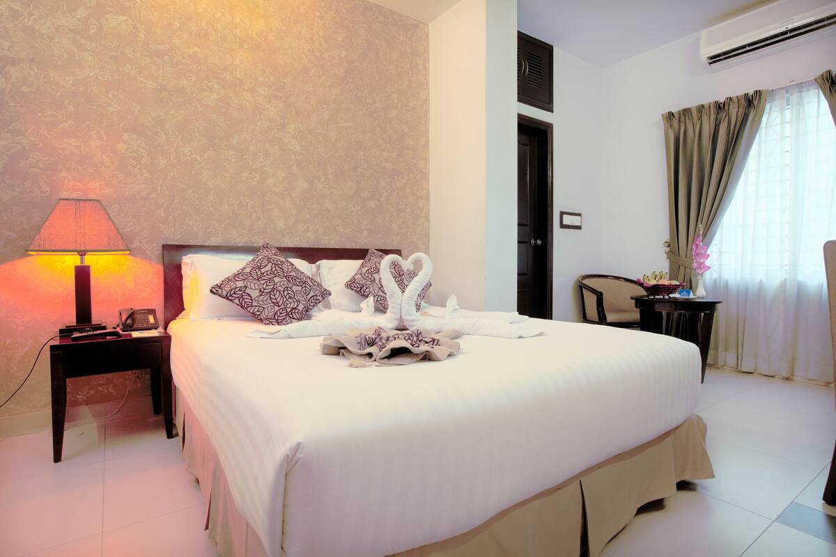 A hotel room with a large bed, a bedside lamp, a telephone, and a chair.