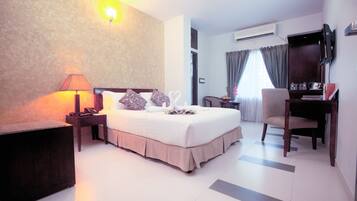 A hotel room with a bed, bedside table, lamp, chair, desk, and TV.