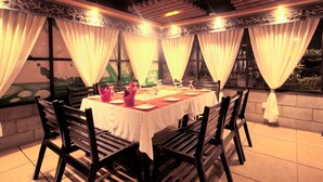 A dining area with a table set for four, surrounded by black chairs, with a view of greenery outside through large windows. - Well Park Residence Boutique Hotel (Chittagong)