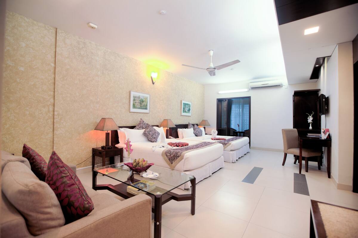 A modern hotel room with a sofa, two beds, a desk, and a TV.