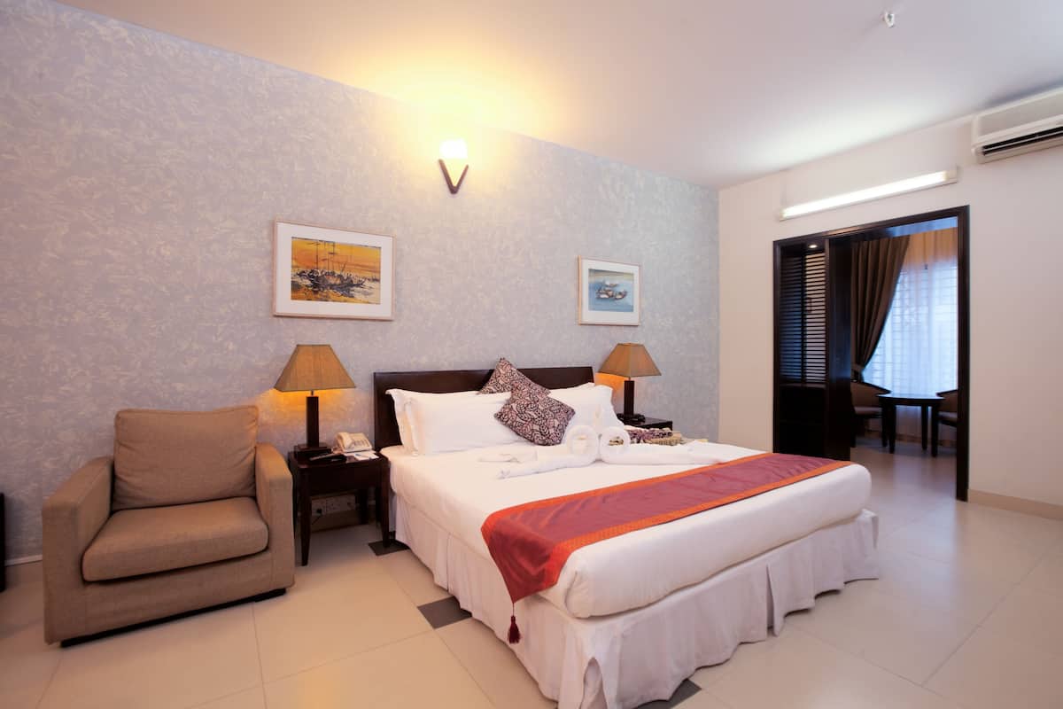 A hotel room with a bed, a chair, two bedside lamps, and two framed pictures on the wall.