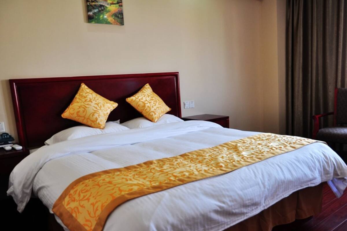 Een hotelkamer met een groot bed, twee decoratieve kussens, een nachtkastje met een telefoon en een stoel.