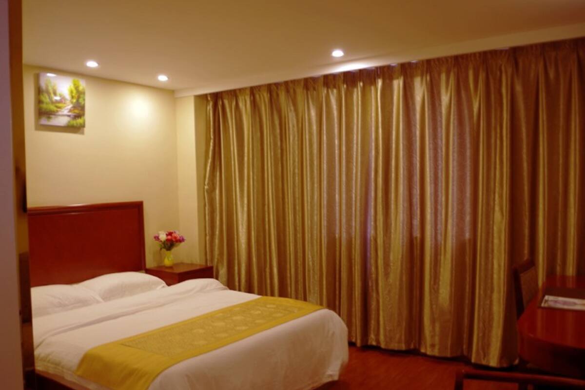 Een hotelkamer met een groot bed, een houten hoofdeinde, een nachtkastje met een bloemenvaas, en een stoel.