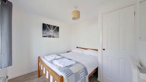 A bedroom with a bed, a door, a wall-mounted light fixture, and a framed picture.