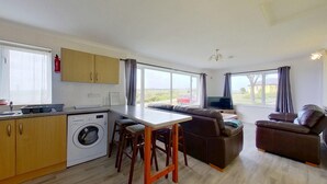 A compact living space with a kitchen, a sofa, a TV, and a washing machine. - D56 Beachcomber, Riviere Towans (Hayle)