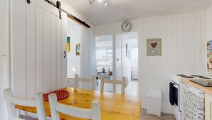 A cozy, well-lit room with a wooden dining table, white chairs, a kitchen area with a stove, and a clock on the wall. - D34 Homeleigh, Riviere Towans (Hayle)