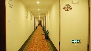 A hotel hallway with a carpeted floor, a sign indicating an elevator, and a wall-mounted emergency exit sign. - Greentree Sunshine 100 Express Hotel (Tianjin)