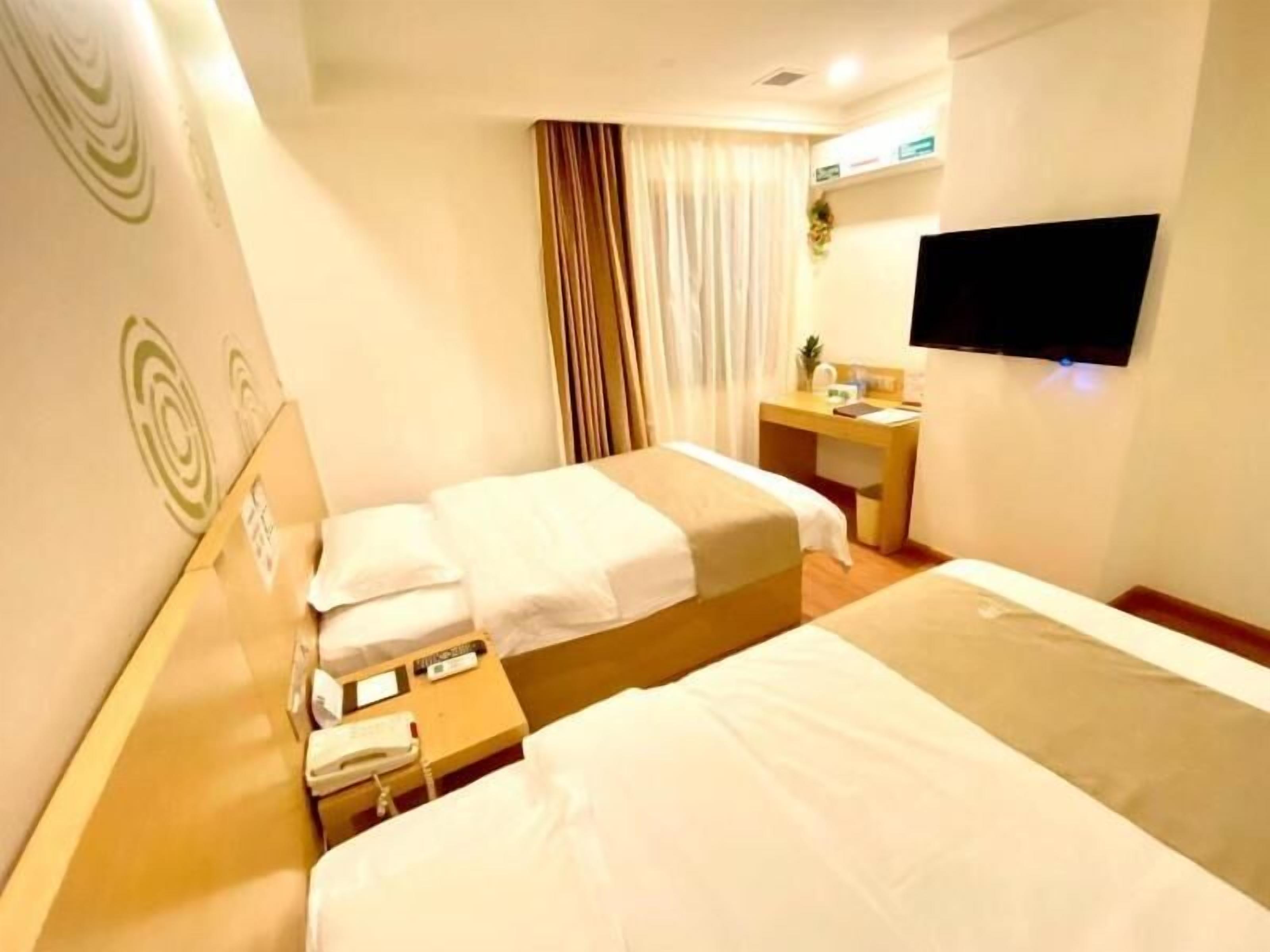 A hotel room with two beds, a desk, a TV, and a window with curtains.