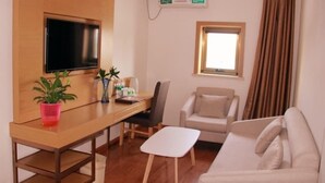 A modern living room with a wooden desk, a flat-screen TV, a sofa, and a chair. - Greentree Sunshine 100 Express Hotel (Tianjin)