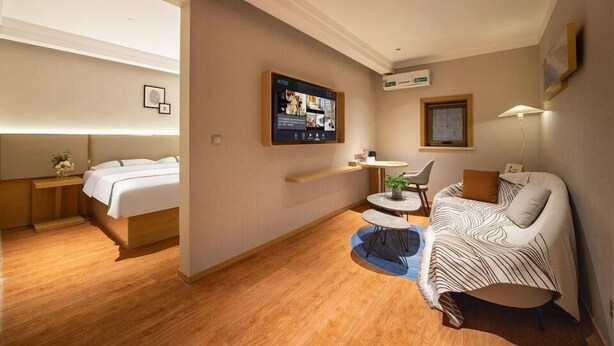 A hotel room with a bed, a sofa, a small table, a TV, and a wall-mounted shelf. - Greentree Sunshine 100 Express Hotel (Tianjin)