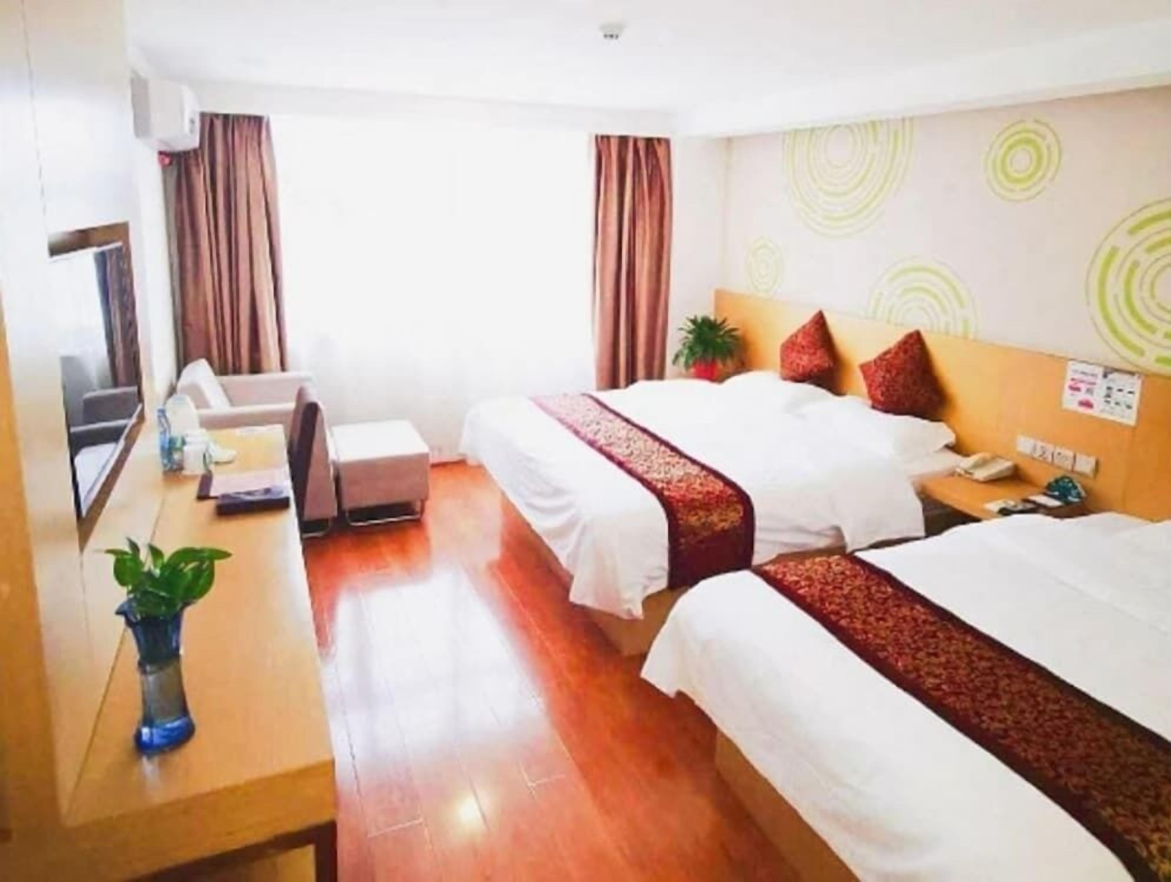 Une chambre d’hôtel avec deux lits, un bureau, une chaise, une petite table et une plante en pot.