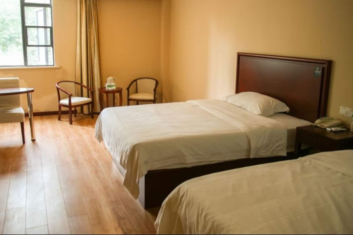 Une chambre d’hôtel avec deux lits, un bureau, deux chaises, une petite table et une fenêtre avec des rideaux.