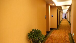 Un couloir d’hôtel avec un sol recouvert de moquette et une plante en pot.