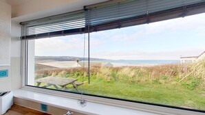 A room with a large window overlooking a grassy area and a beach. - B25 Trezaren, Riviere Towans (Hayle)