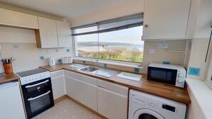 A compact kitchen with a built-in oven, a microwave, a sink, and a washing machine. - B25 Trezaren, Riviere Towans (Hayle)