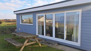 A modern house with a sliding glass door, a wooden bench, and a grassy yard. - B25 Trezaren, Riviere Towans (Hayle)