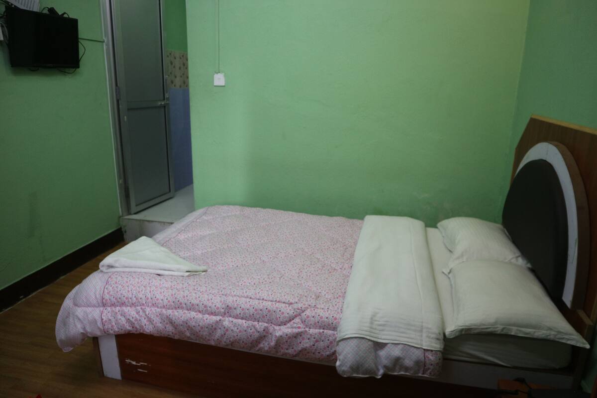 A single bed with a wooden frame, a white mattress, and a pink floral bedspread.
