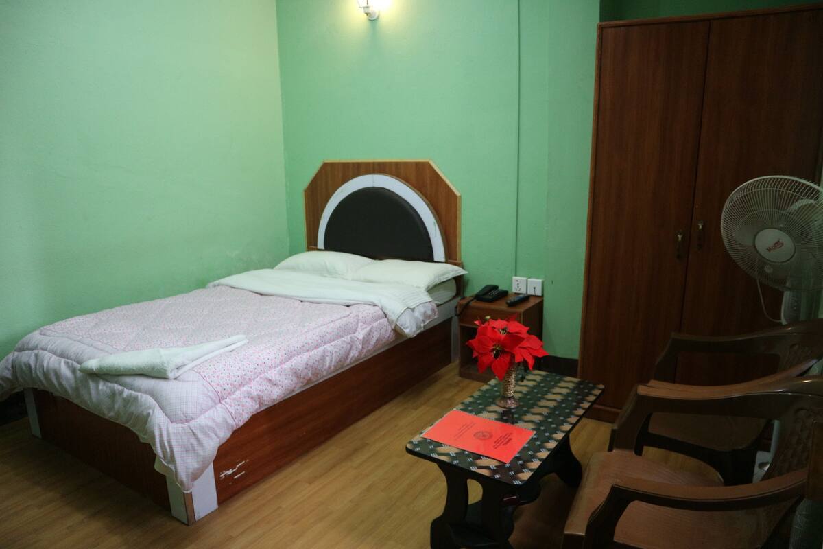 A bedroom with a bed, a nightstand, a table with a vase, a chair, and a wardrobe.