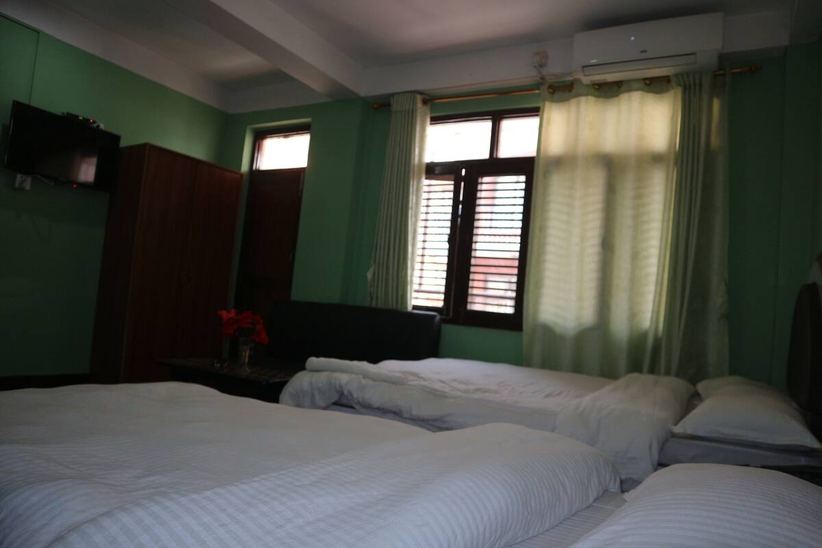 A room with two beds, a television on a stand, and a window with curtains.