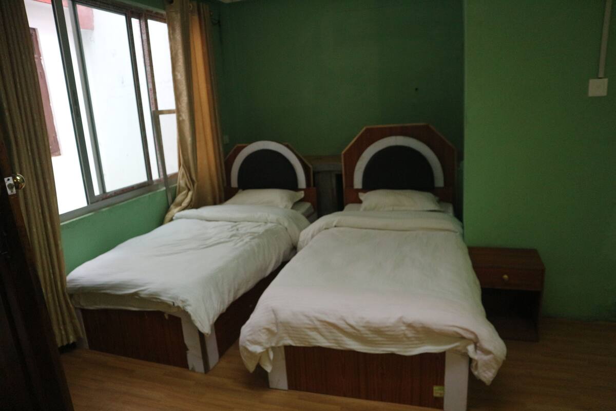 A room with two single beds, a small wooden nightstand, and a window with curtains.