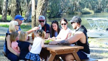 A family dining at a wooden picnic table by a lake.