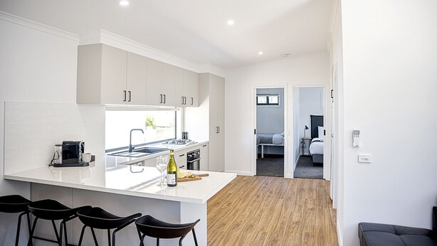 Een moderne keuken met witte kasten, een groot eiland met barkrukken, en uitzicht op een slaapkamer.