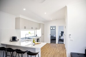 Eine moderne Küche mit weißen Schränken, einer großen Kochinsel mit Barhocker und Blick in ein Schlafzimmer.