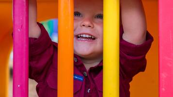 A child climbing a brightly colored play structure with pink, orange, and yellow bars.