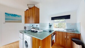 A compact kitchen with wooden cabinets, a washing machine, a microwave, and a toaster.