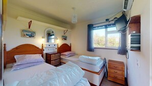 Ein Schlafzimmer mit zwei Betten, einem Holzkopfende, einem Nachttisch, einer Kommode, einem Fenster mit Vorhängen und Wanddekorationen.