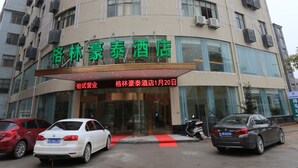 Un hotel con fachada moderna, con amplias ventanas y unidades de aire acondicionado. Hay coches aparcados delante y una alfombra roja que conduce a la entrada.