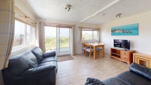 A spacious living area with a sofa, a dining table, and a television. - C37 Jupiter, Riviere Towans (Hayle)