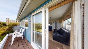 A covered outdoor area with a wooden deck, white plastic chairs, and a black leather sofa. - C37 Jupiter, Riviere Towans (Hayle)