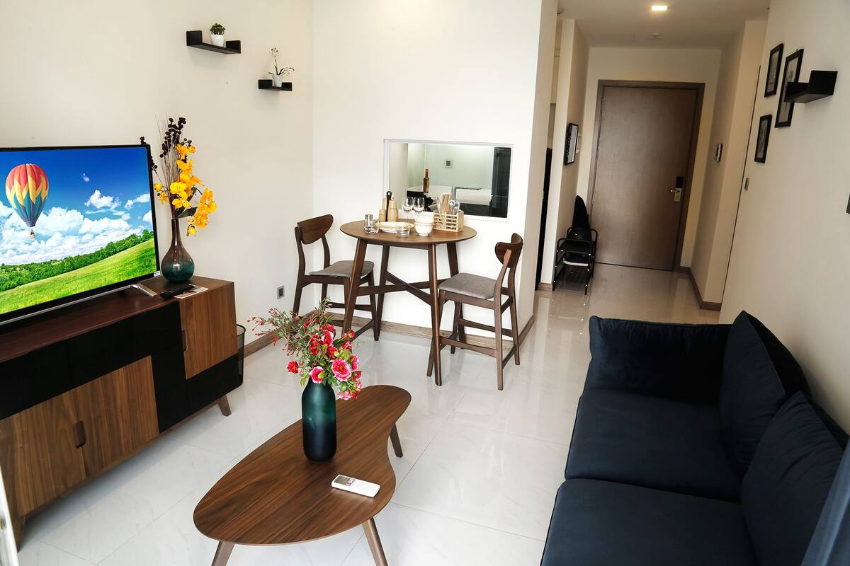Een moderne woonkamer met een flatscreen televisie, een salontafel met een bloevas, een bank en een eethoek met stoelen en een tafel.