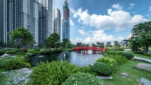 Ein Park mit einem Teich, einer roten Brücke und hohen Gebäuden im Hintergrund.