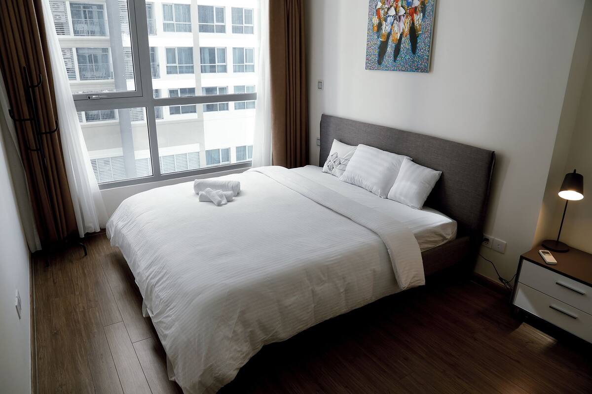 Een opgemaakt bed met witte lakens, een hoofdbord en een nachtkastje met een lamp.