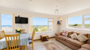Una sala de estar con televisor, mesa de comedor, sillas, sofá y ventanas amplias con vistas.