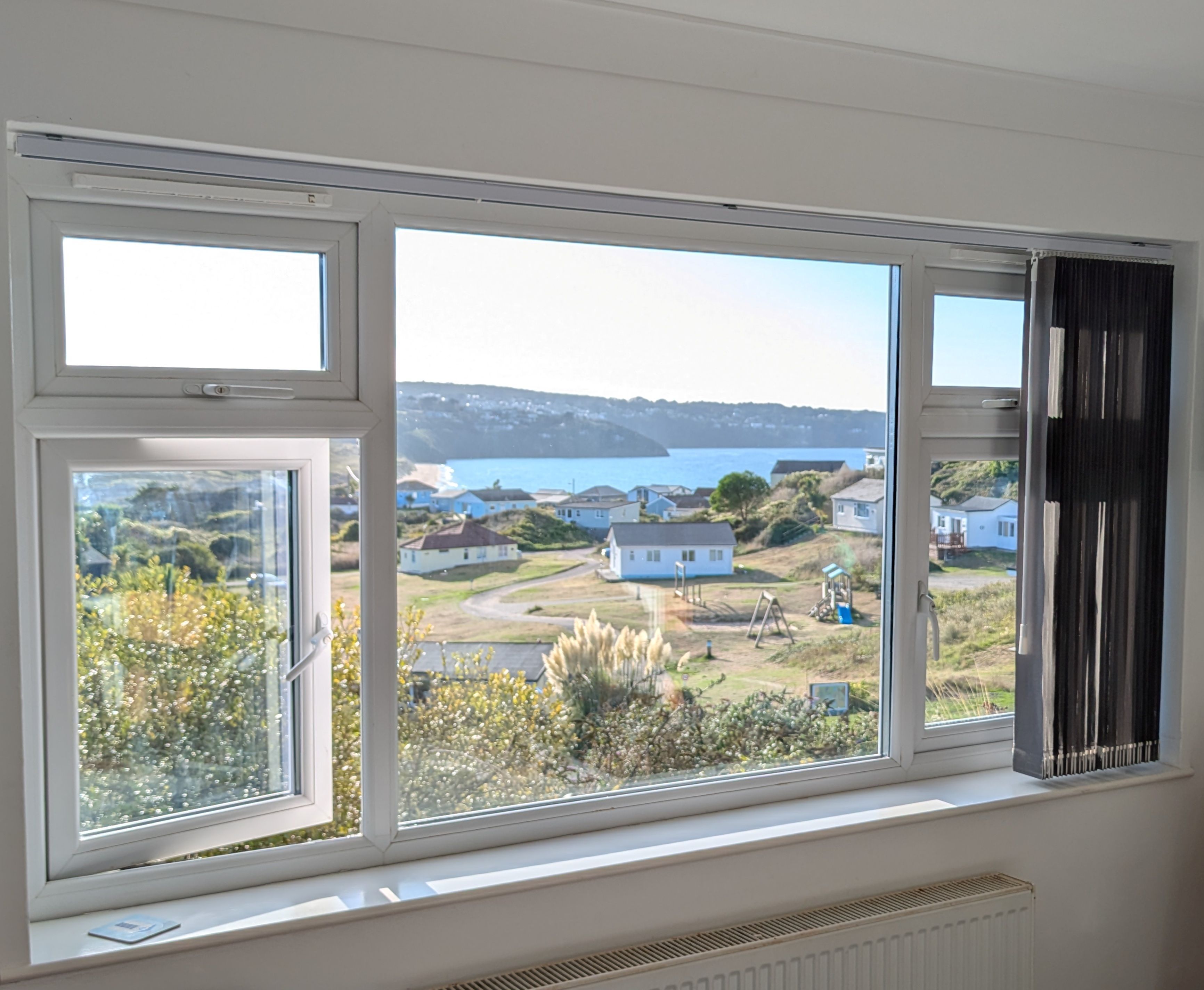 A room with a large window overlooking a coastal area with houses and a body of water.