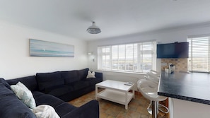 A modern living room with a dark sofa, a white coffee table, and a painting on the wall.