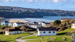 A coastal residential area with houses, a beach, and a hill in the background. - E29 Bonnie Bank, Riviere Towans (Hayle)