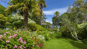 A lush garden with a variety of flowering plants, a well-maintained lawn, and a conservatory. - Chapel Knap, Porlock Weir (Porlock Weir)