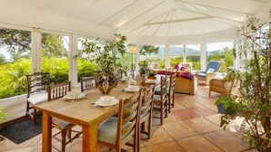 A conservatory with a dining table set for four, surrounded by wicker furniture and potted plants. - Chapel Knap, Porlock Weir (Porlock Weir)