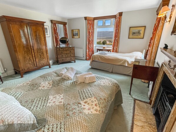 Een slaapkamer met een groot bed, een dressoir, een bureau en een open haard.