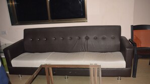 A brown sofa with a white cushion, a wooden coffee table, and a chair with an orange backrest. - Hotel cloud 9 (Madhubani)
