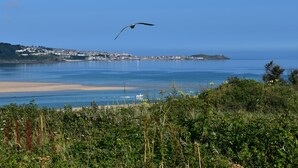 A coastal landscape with a clear view of the sea, a sandy beach, and a distant town. - C20 Y Worry, Riviere Towans (Hayle)
