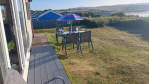A patio with a table and chairs, a blue umbrella, and a view of the countryside. - C20 Y Worry, Riviere Towans (Hayle)